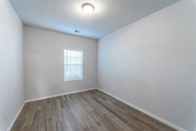 a view of an empty room with wooden floor and window