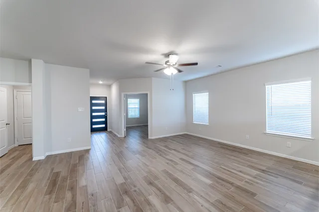 an empty room with wooden floor chandelier fan and windows