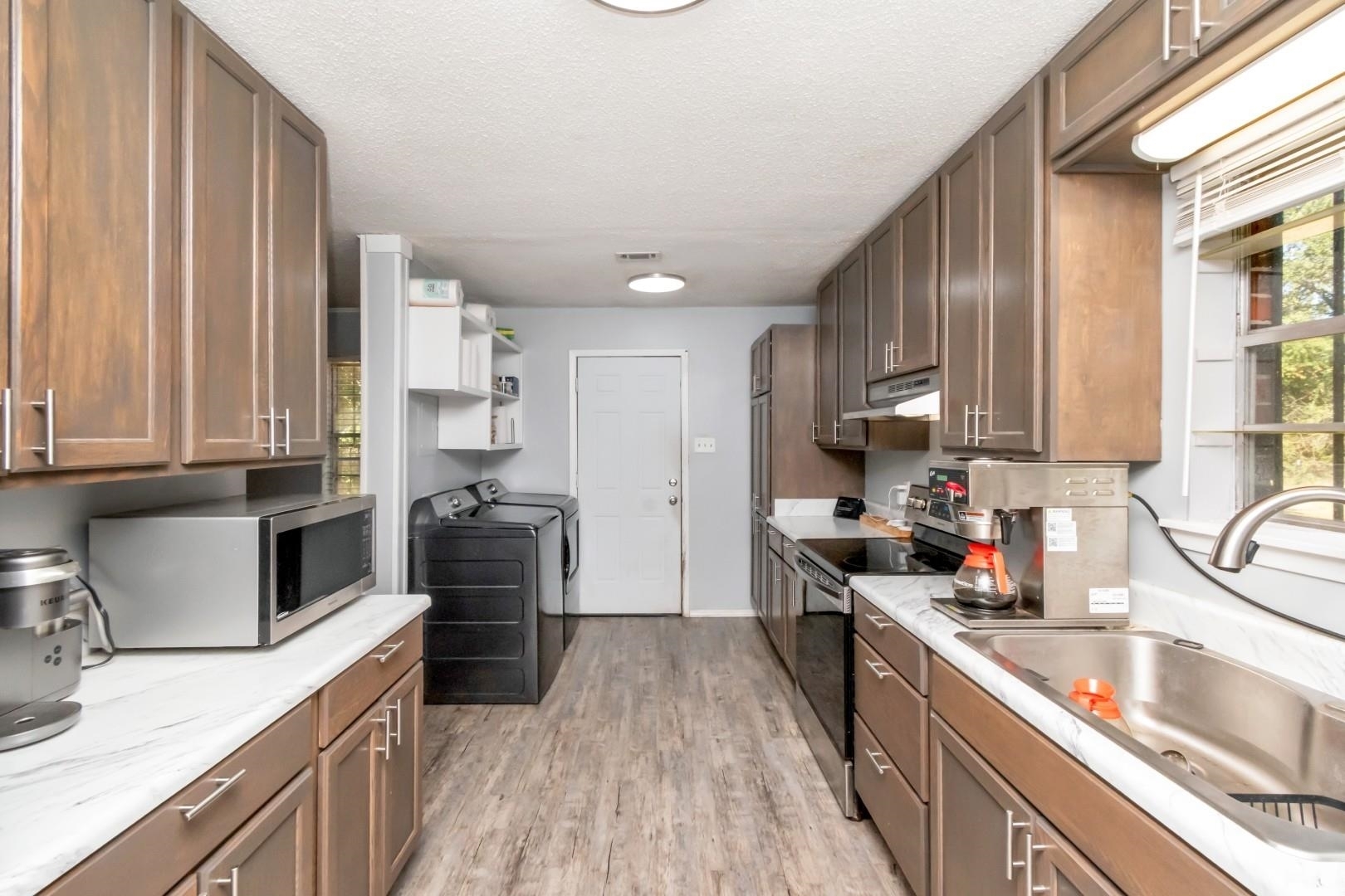 6405 1st Street Wilmer, AL 36587 - Photo 10 of 38 Kitchen featuring stainless steel appliances, light wood finished floors, a textured ceiling, washing machine and dryer, and open shelves