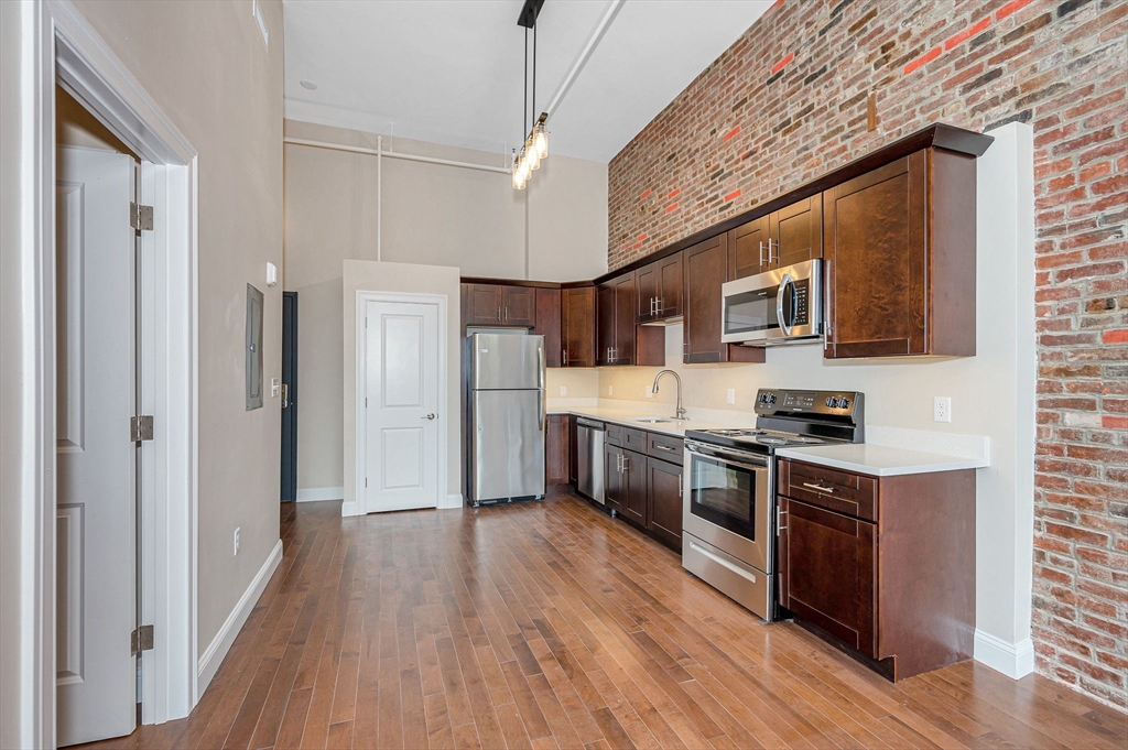 231 Central Street, Unit 203 Lowell, MA 01852 - Photo 7 of 15 a kitchen with stainless steel appliances wooden floors and wooden cabinets