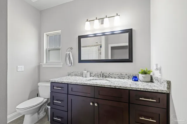 a bathroom with a granite countertop sink vanity mirror and toilet