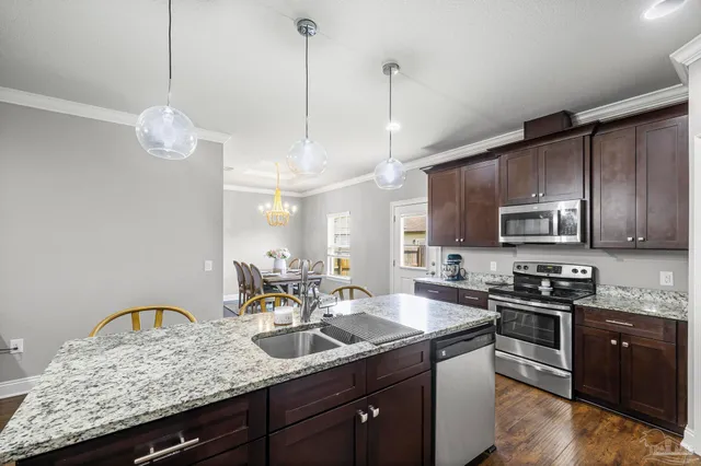 a kitchen with granite countertop stainless steel appliances a sink a stove a counter space cabinets and wooden floor