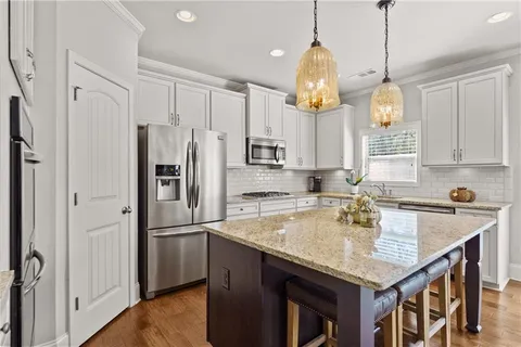 a kitchen with stainless steel appliances granite countertop a stove top oven a refrigerator a sink and white cabinets with wooden floor