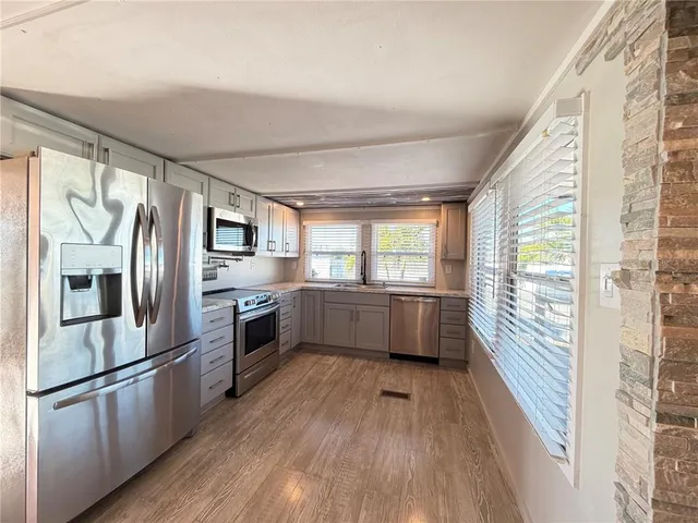 a kitchen with stainless steel appliances a refrigerator a sink a stove and white wooden cabinets with wooden floor