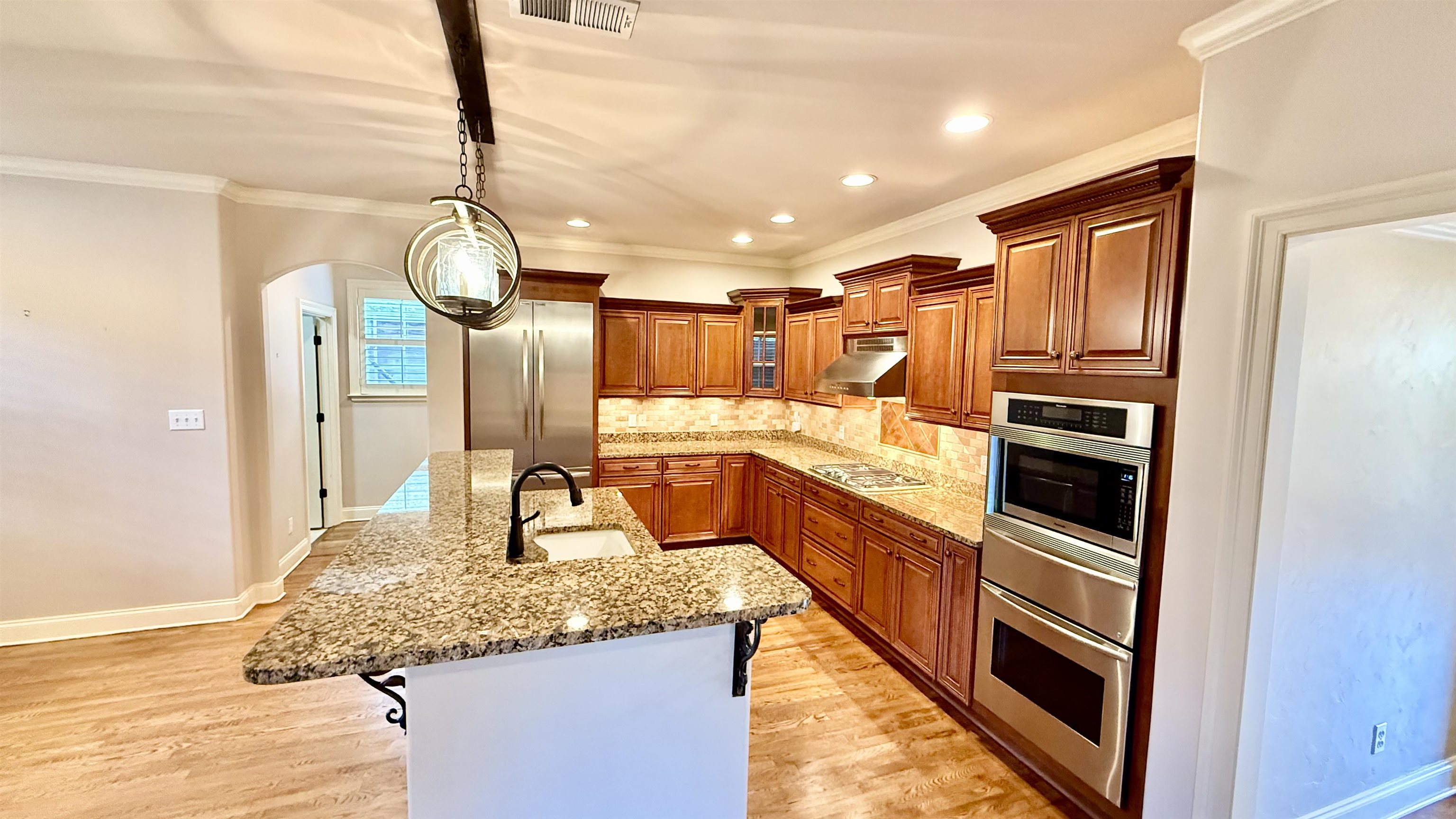 247 South Greer Street Memphis, TN 38111 - Photo 7 of 29 Kitchen featuring arched walkways, ornamental molding, decorative backsplash, glass insert cabinets, and light stone counters