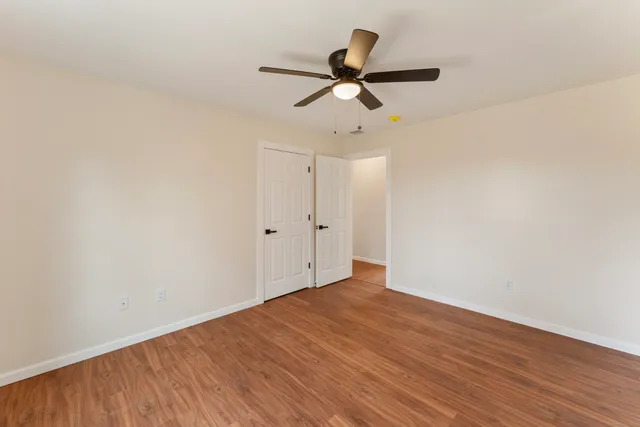 an empty room with wooden floor ceiling fan and windows