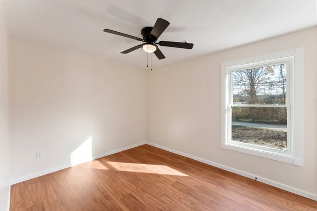 an empty room with wooden floor ceiling fan and windows