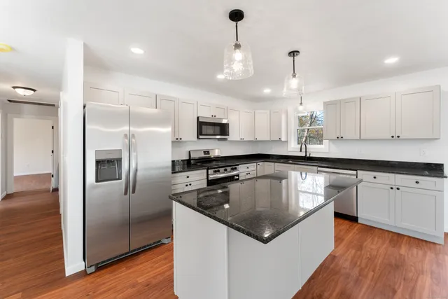 a kitchen with stainless steel appliances granite countertop a sink a stove a refrigerator and island with wooden floor