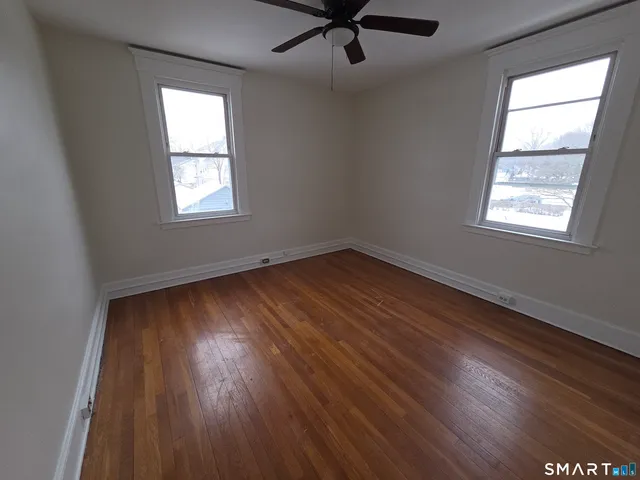 an empty room with wooden floor windows and fan