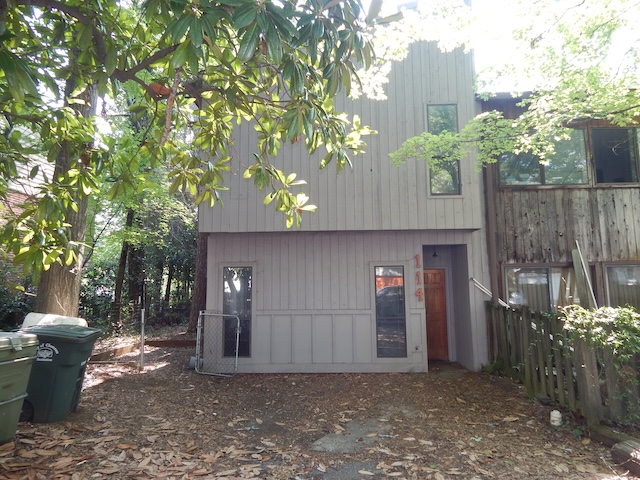 A private entry leads to a home with textured wood siding, nestled amongst mature trees.