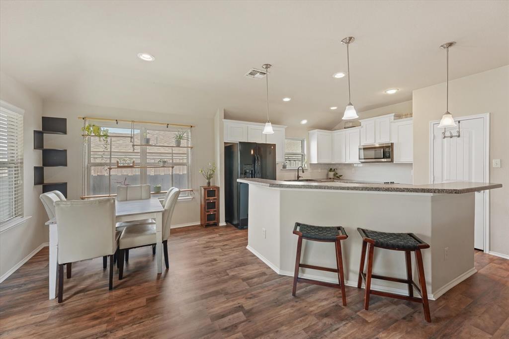 409 Harding Lane Lavon, TX 75166 - Photo 20 of 34 Open-concept dining area and kitchen featuring wood-finish flooring, white cabinetry, integrated stainless steel microwave, and pendant lighting over a breakfast bar