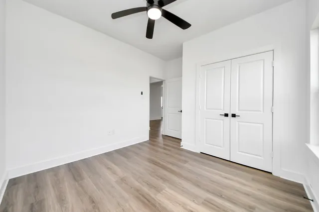 an empty room with wooden floor ceiling fan and windows