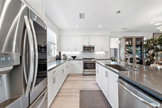 a large kitchen with stainless steel appliances granite countertop a refrigerator a sink and white cabinets