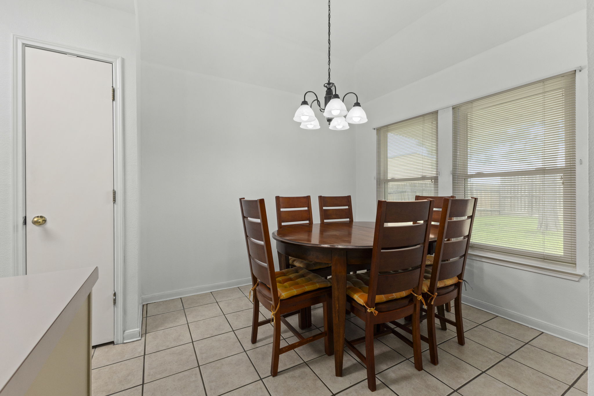290 Bailey Loop Kyle, TX 78640 - Photo 14 of 33 Dining area featuring a dark bronze chandelier with five frosted glass shades, two large windows with blinds, and light-toned square tile flooring