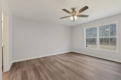 an empty room with wooden floor chandelier fan and windows