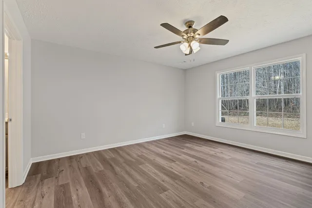 an empty room with wooden floor chandelier fan and windows