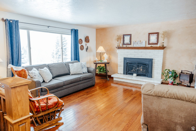 322 Bailey Creek Road Soda Springs, ID 83276 - Photo 5 of 32 Living area featuring wood-finish flooring, a white brick fireplace with a dark metal insert, and a large picture window