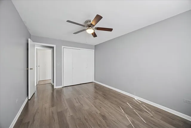 a view of an empty room with wooden floor and a ceiling fan