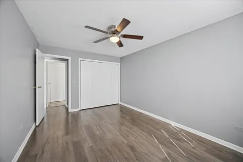 a view of an empty room with wooden floor and a ceiling fan