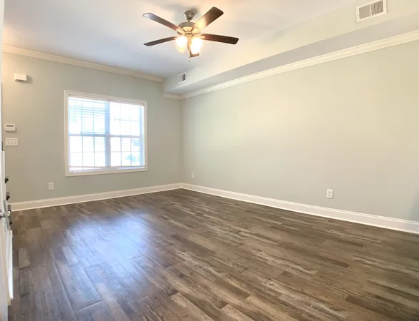 an empty room with wooden floor fan and windows