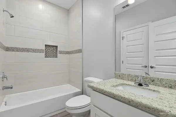 a bathroom with a granite countertop bathtub sink vanity mirror and toilet