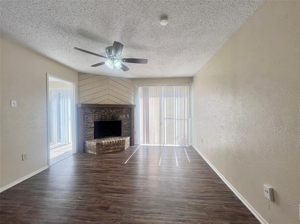 an empty room with wooden floor a ceiling fan a fireplace and windows
