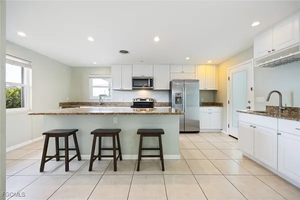 a kitchen with granite countertop white cabinets a sink a stove a oven with dining table and chairs