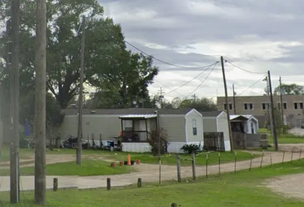 a view of a white house in front of a big yard with plants and large trees