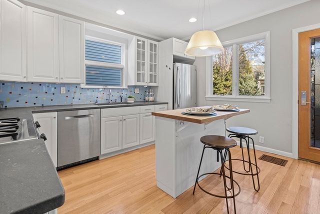 a kitchen with stainless steel appliances granite countertop a stove a sink dishwasher and white cabinets with wooden floor