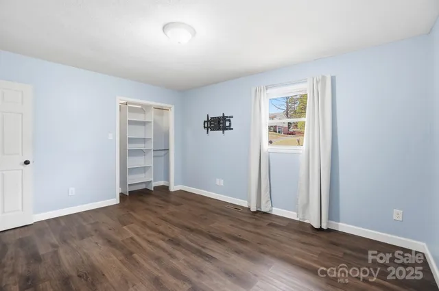 an empty room with wooden floor closet and windows