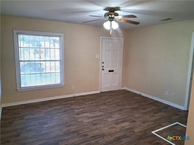 a view of an empty room with wooden floor and a window