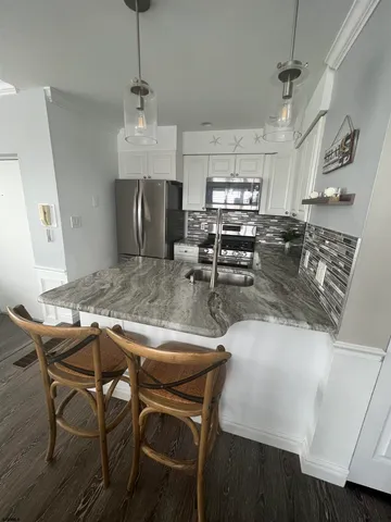 a kitchen with stainless steel appliances granite countertop a stove top oven a refrigerator a sink and chairs