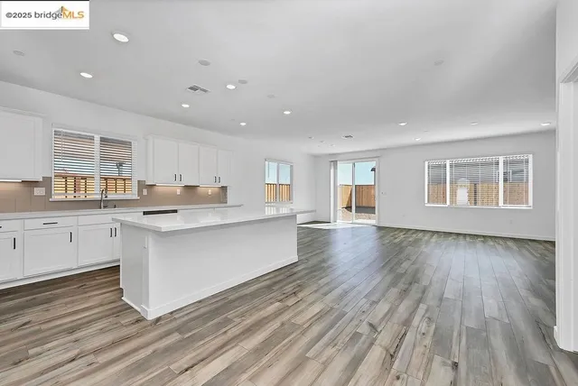 a large white kitchen with kitchen island a sink dishwasher a stove and a dining table with wooden floor