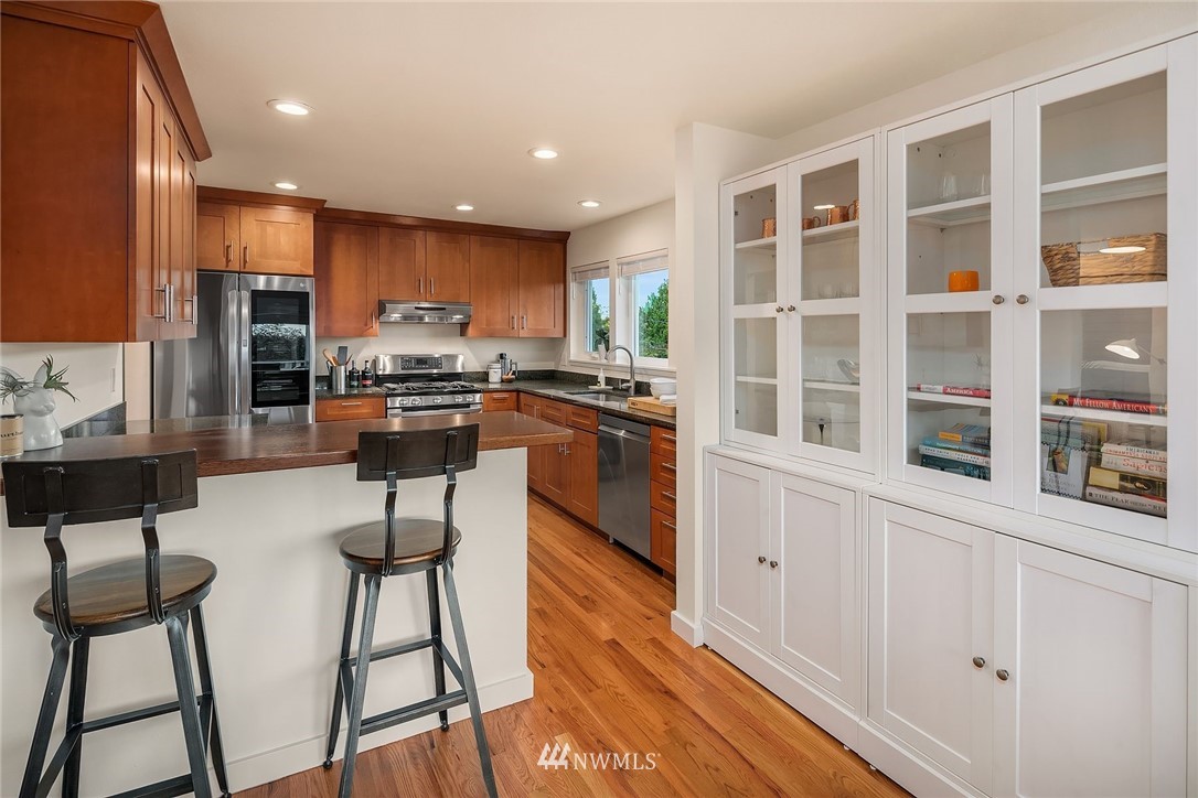 355 North 75th Street Seattle, WA 98103 - Photo 14 of 32 a kitchen with stainless steel appliances kitchen island granite countertop a stove a refrigerator a sink a dining table and chairs with wooden floor