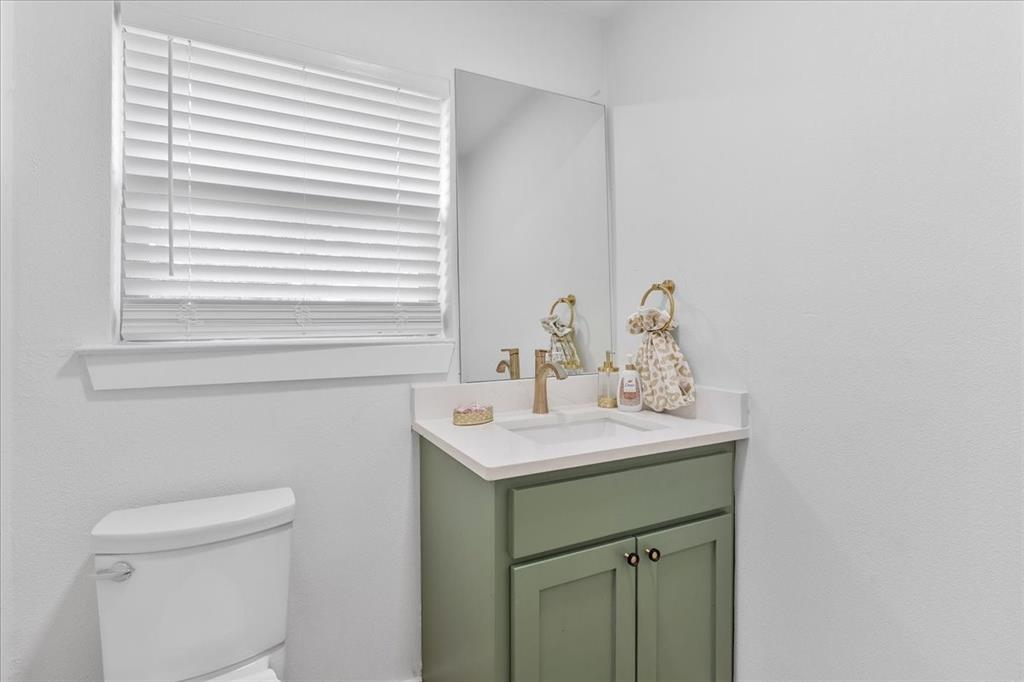 3509 West Sublett Road Arlington, TX 76017 - Photo 18 of 39 White wall-mounted toilet, vanity with sage green cabinetry, white countertop, integrated sink, and a rectangular mirror