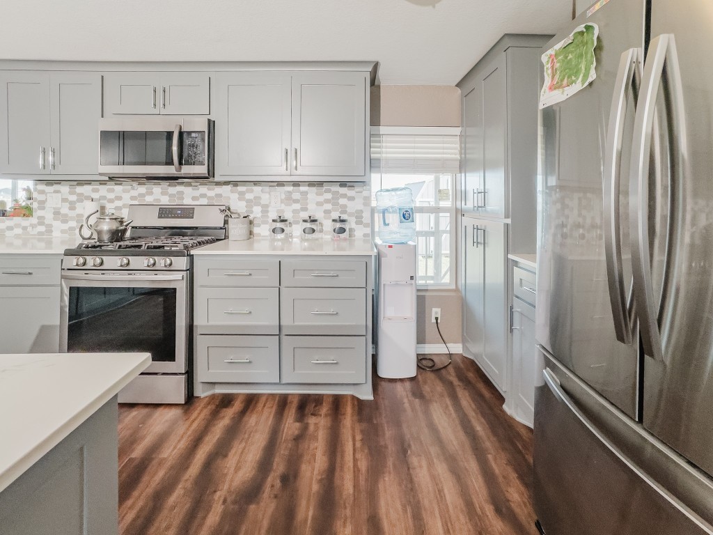 2709 County Road 463 Elgin, TX 78621 - Photo 19 of 40 Kitchen featuring stainless steel appliances, gray cabinets, tasteful backsplash, dark wood-style flooring, and light stone countertops