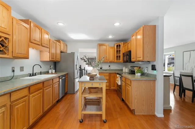 a kitchen with stainless steel appliances granite countertop wooden cabinets a sink dishwasher a stove and a refrigerator with wooden floor