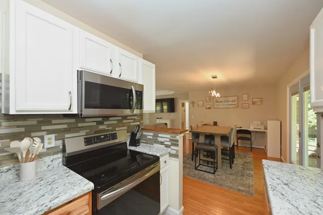 a kitchen with stainless steel appliances granite countertop a stove top oven a sink a dining table and chairs with wooden floor