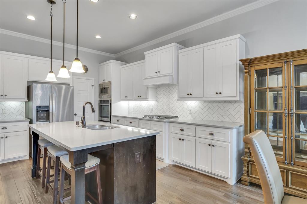 1306 Elizabeth Street Anna, TX 75409 - Photo 25 of 36 Kitchen featuring white cabinetry, a center island with sink, dark brown cabinetry, decorative light fixtures, and crown molding