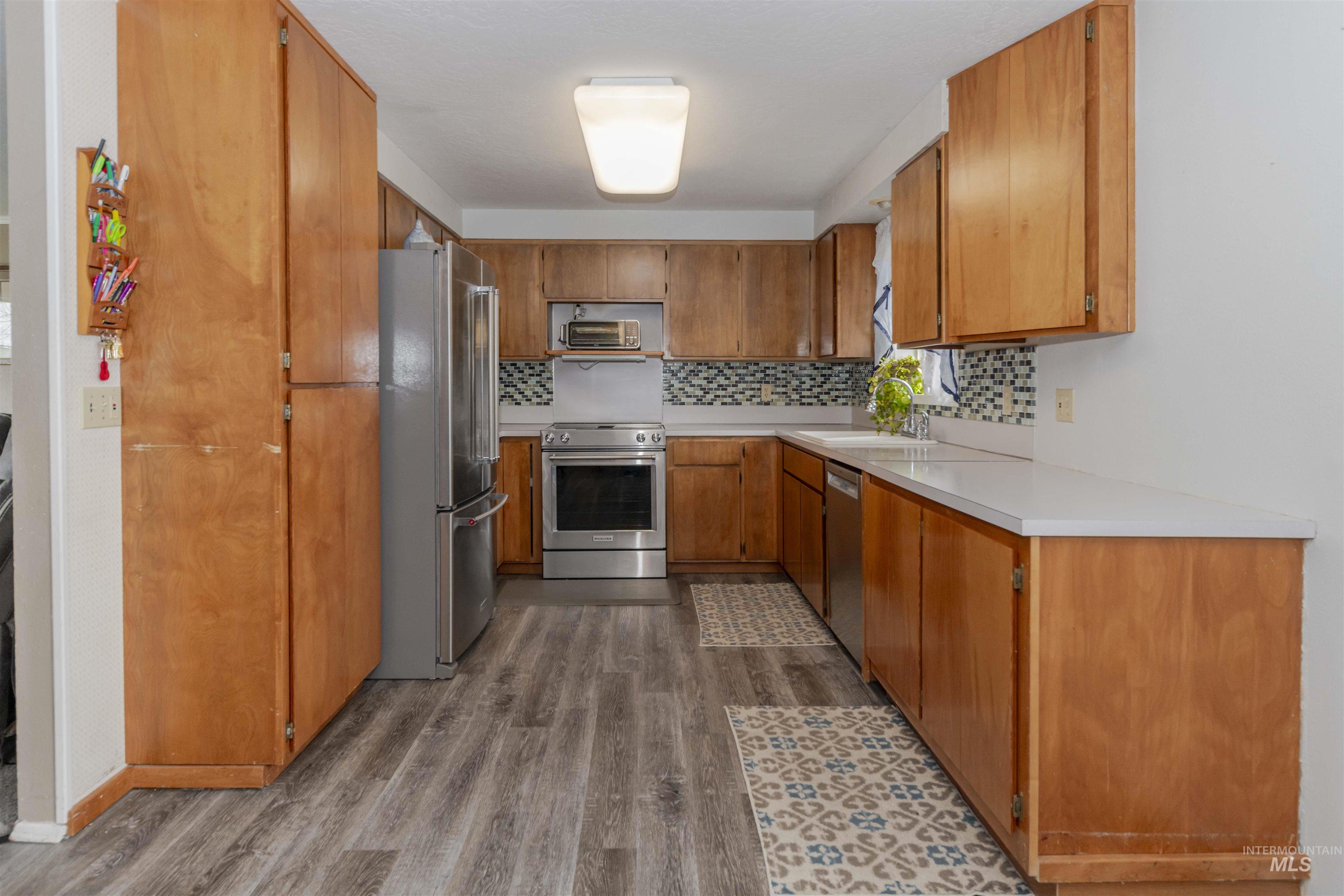 930 Preston Avenue Lewiston, ID 83501 - Photo 5 of 32 Kitchen with brown cabinets, light countertops, appliances with stainless steel finishes, dark wood finished floors, and decorative backsplash