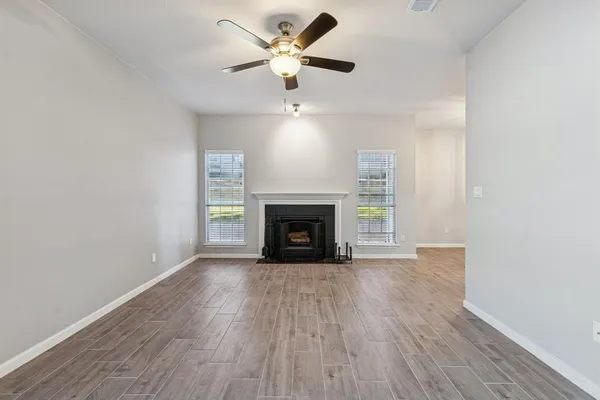 a view of an empty room with wooden floor a fireplace and a window