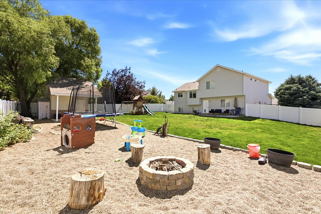 2247 South 425 West Perry, UT 84302 - Photo 26 of 29 Spacious backyard featuring a stone-ringed fire pit on a gravel base, a manicured lawn, a white vinyl fence, mature trees, and a detached shed