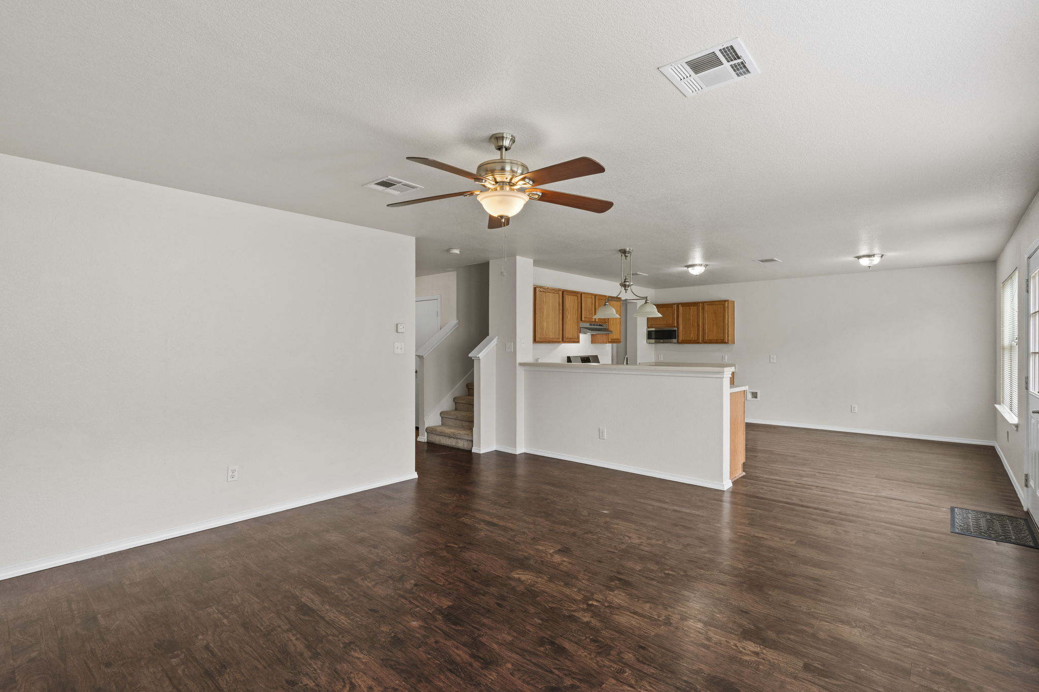 208 Dandelion Loop Kyle, TX 78640 - Photo 16 of 39 Expansive living area featuring LVT wood-look flooring, a ceiling fan with light fixture, and an open concept layout to the kitchen with wood cabinetry