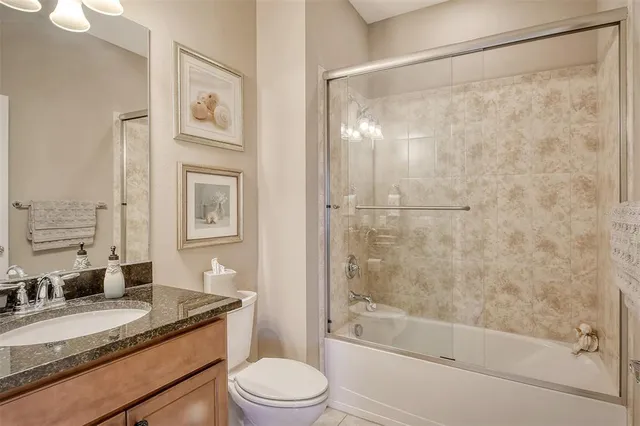 a bathroom with a granite countertop bathtub shower sink vanity and toilet
