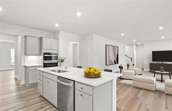 a kitchen with stainless steel appliances a stove a sink a refrigerator white cabinets and couches with wooden floor