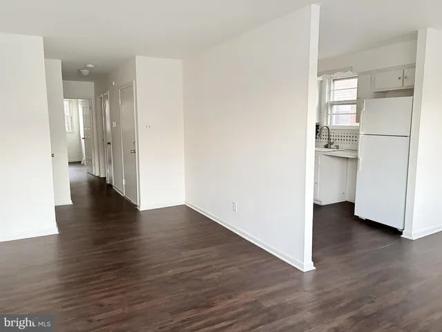 a view of an empty room with wooden floor and a kitchen