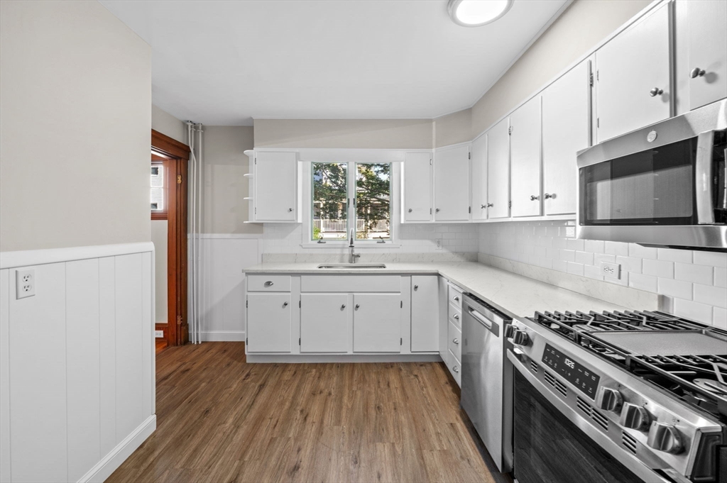 59 Butman Street, Unit 1 Beverly, MA 01915 - Photo 7 of 42 a kitchen with granite countertop a stove top oven a sink dishwasher and white cabinets with wooden floor