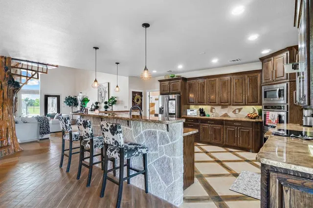 a kitchen with stainless steel appliances granite countertop a stove top oven a refrigerator a sink and a dining table with wooden floor