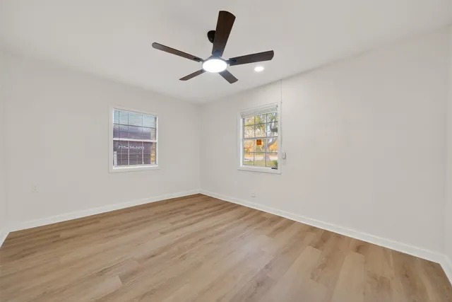 an empty room with wooden floor ceiling fan and windows