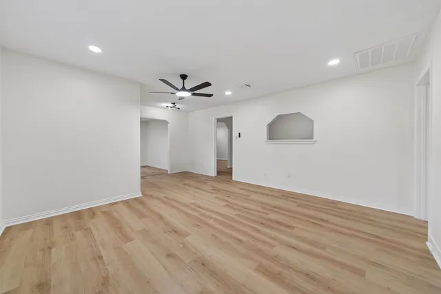 a view of an empty room with wooden floor and a ceiling fan
